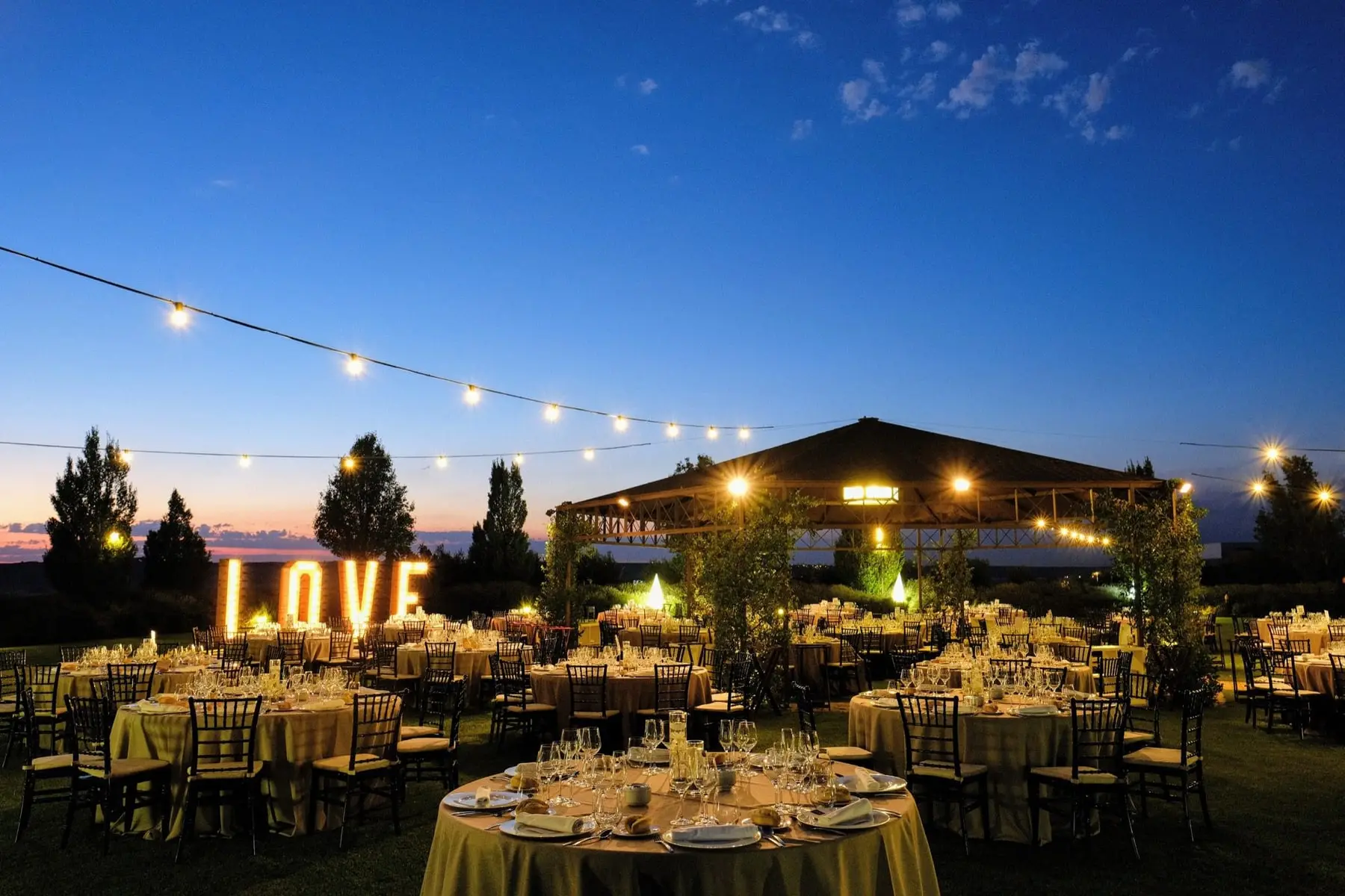 Cena en el jardín al anochecer, con las letras LOVE encendidas y guirnaldas sobre las mesas