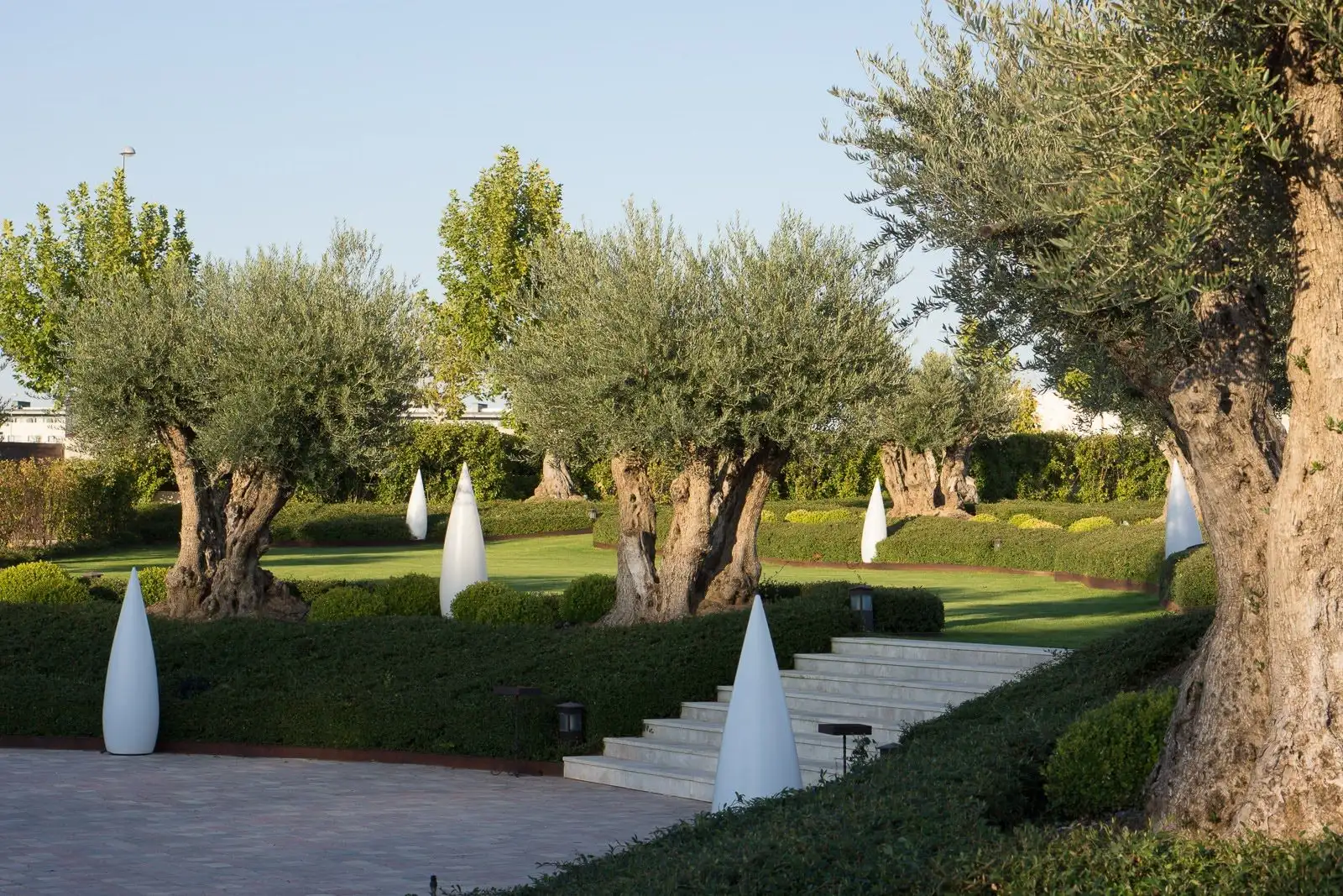 Olivos y setos a distintos niveles en el Jardín del Mirador, con una escalera de piedra y lámparas blancas