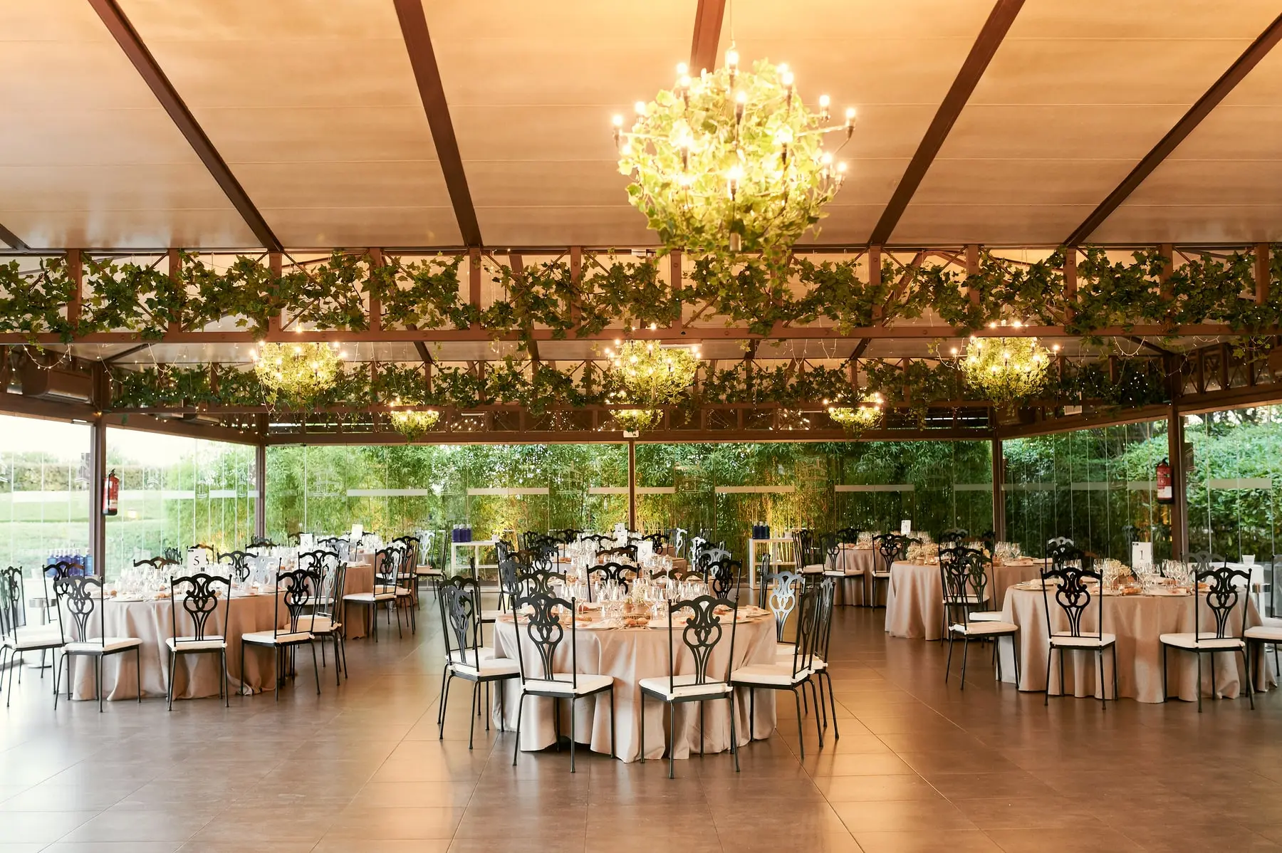 El salón de cristal del Mirador con arañas de hojas, vigas de madera y mesas redondas puestas